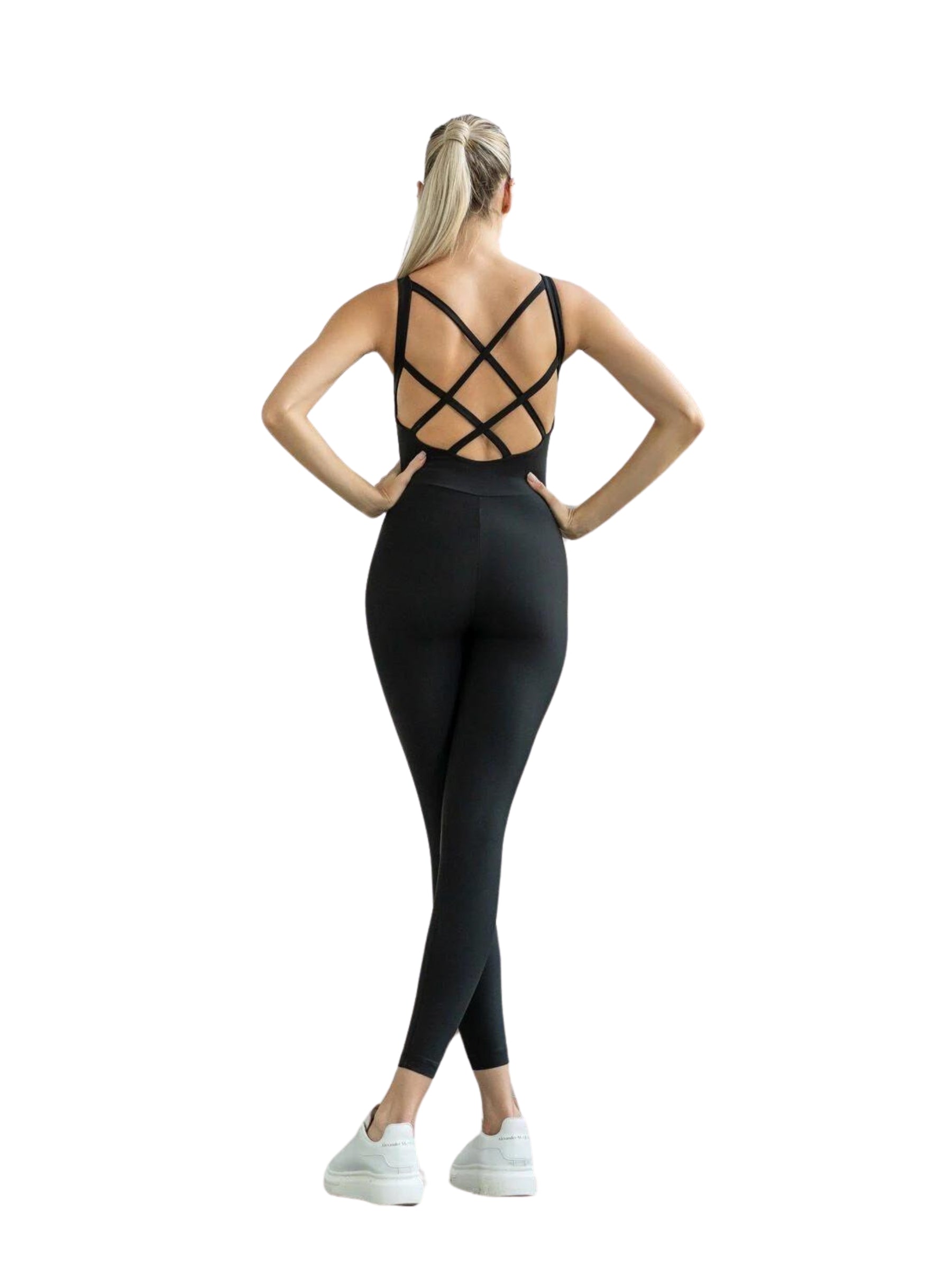 Person im Lismina 2100 Double Cross Jumpsuit, steht mit in die Hüften gestemmten Armen und trägt weiße Turnschuhe.
